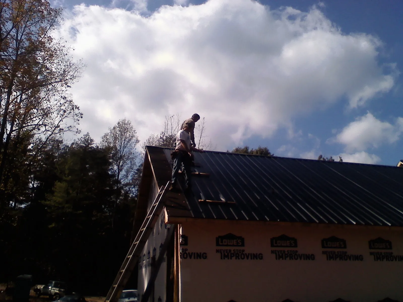 Roofer fastening dark metal panels high against a cloudy sky, from a Roof Inspection job in Jbsa Ft Sam Houston