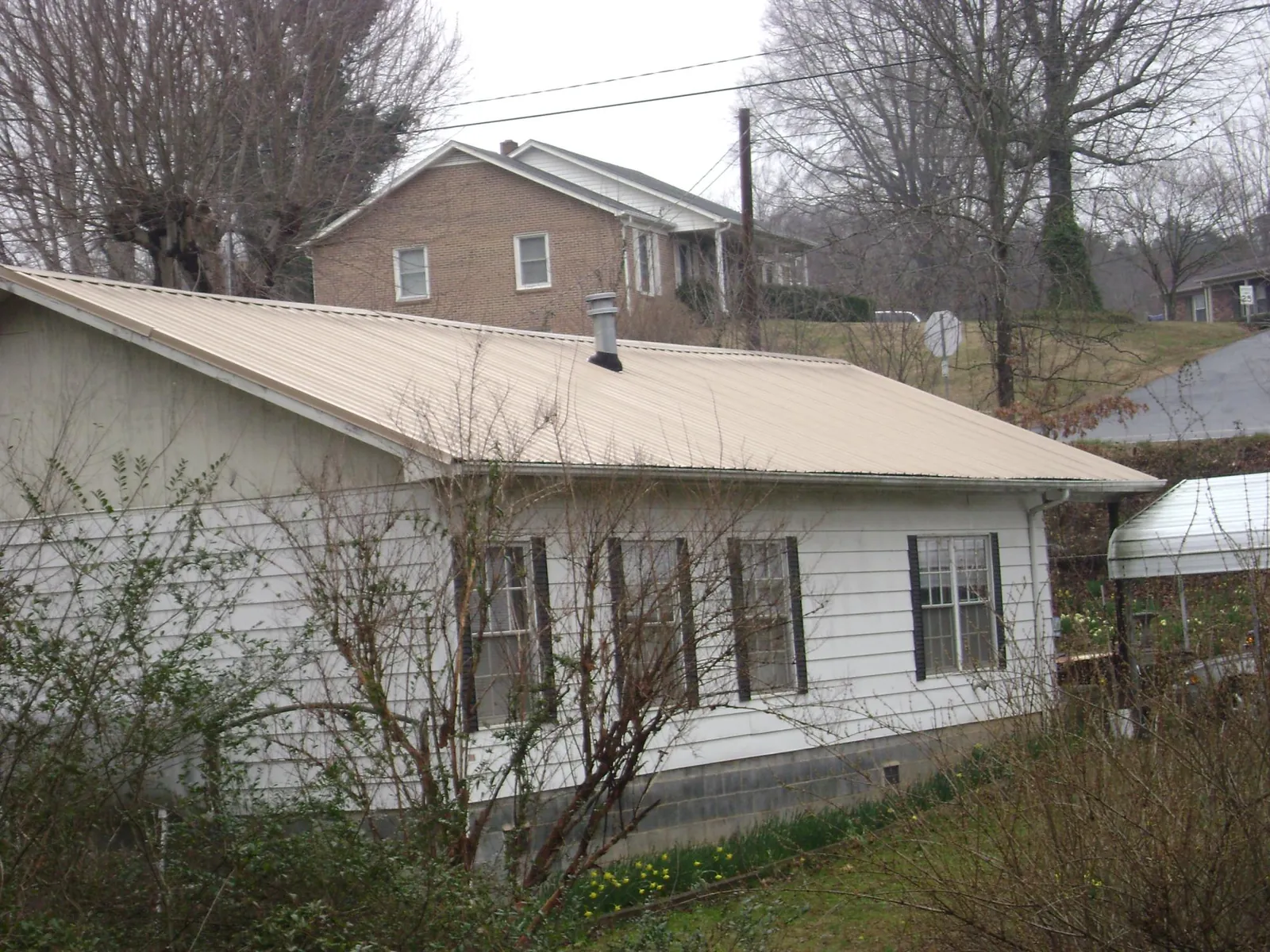 Tan metal roof on a white sided house set into a hillside — Commercial Roofing by Roofing Brothers in Jbsa Ft Sam Houston